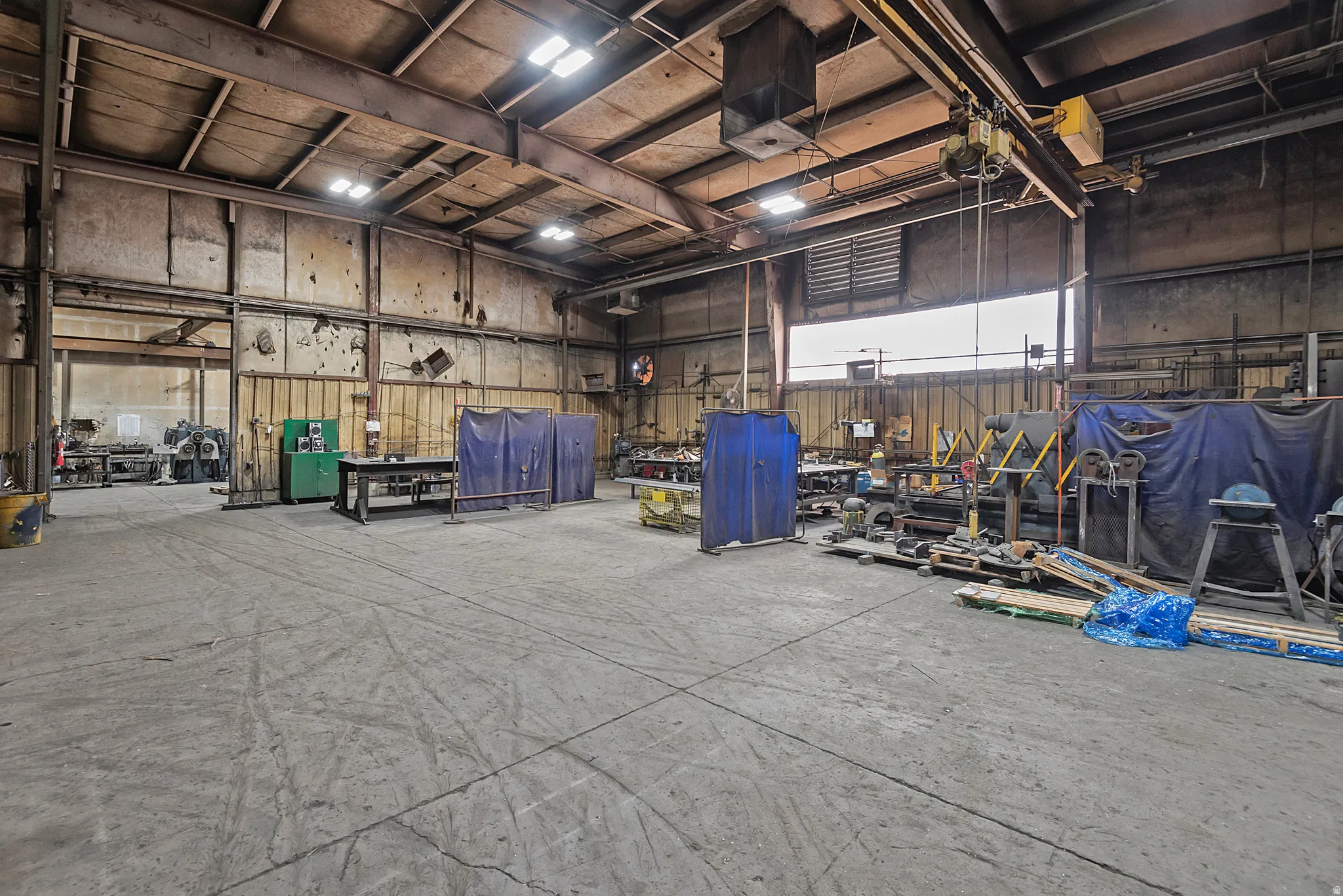 Industrial warehouse space featuring high ceilings, exposed structural beams, overhead lighting, and an overhead crane system