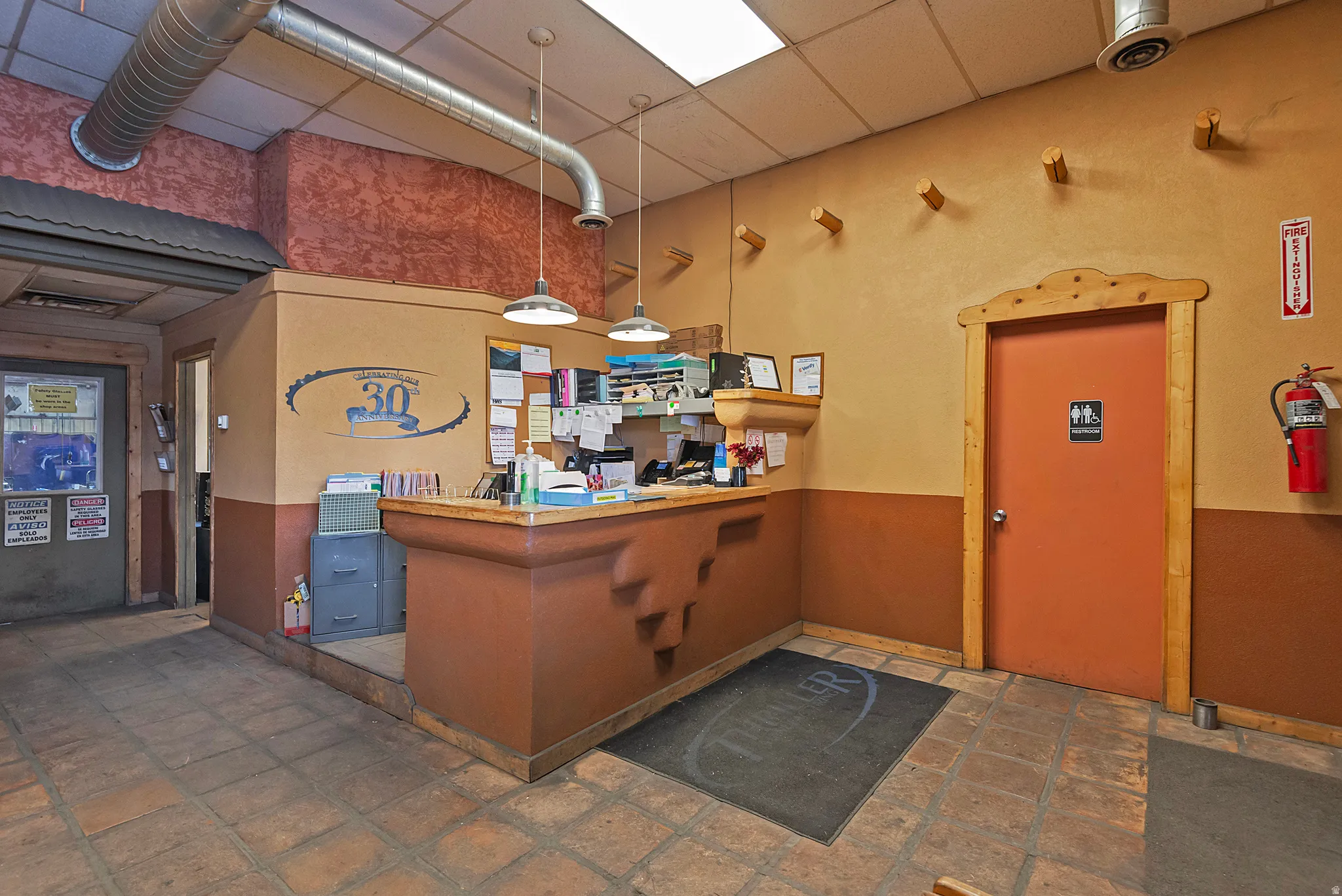 Terracotta tile flooring, exposed ductwork, drop ceiling with fluorescent lighting, built-in reception desk, and solid core doors with wood trim
