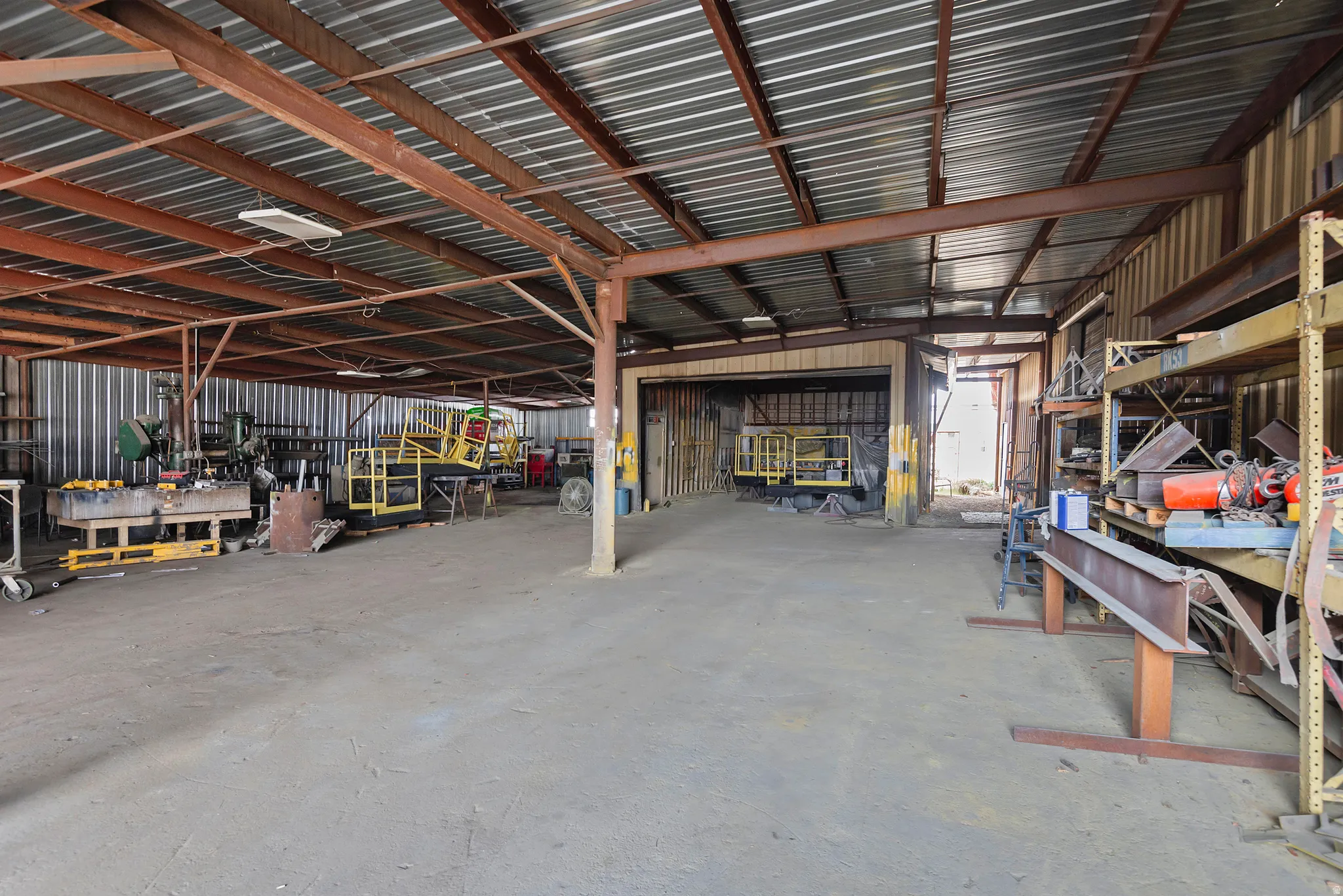 Steel beam construction with corrugated metal roofing, concrete flooring, and ample overhead lighting