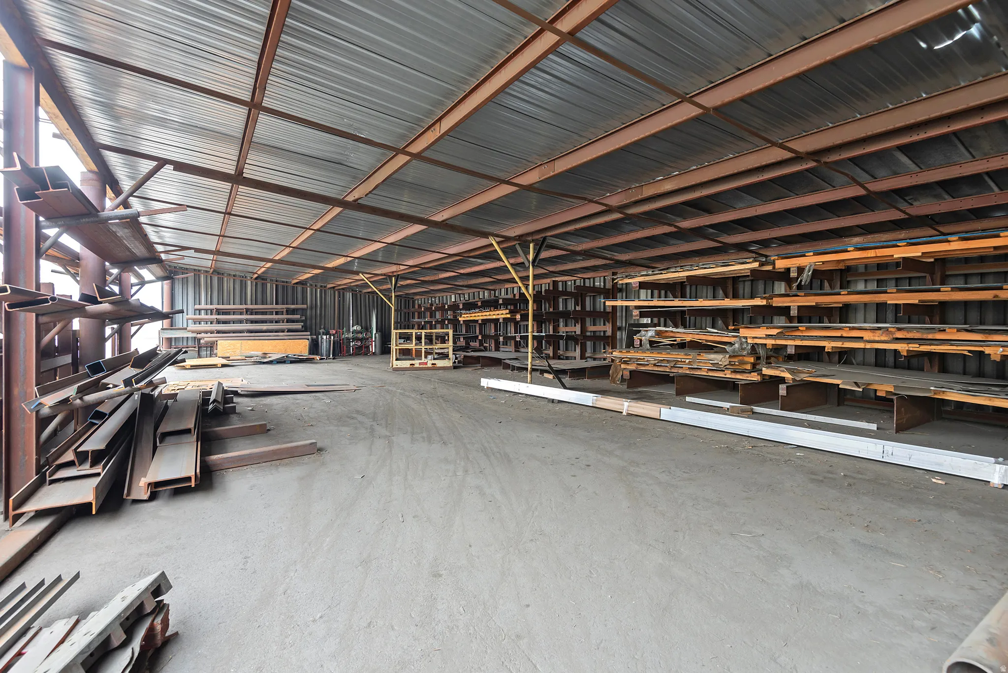 Covered structure featuring a corrugated metal roof, exposed metal beam framework, and concrete flooring