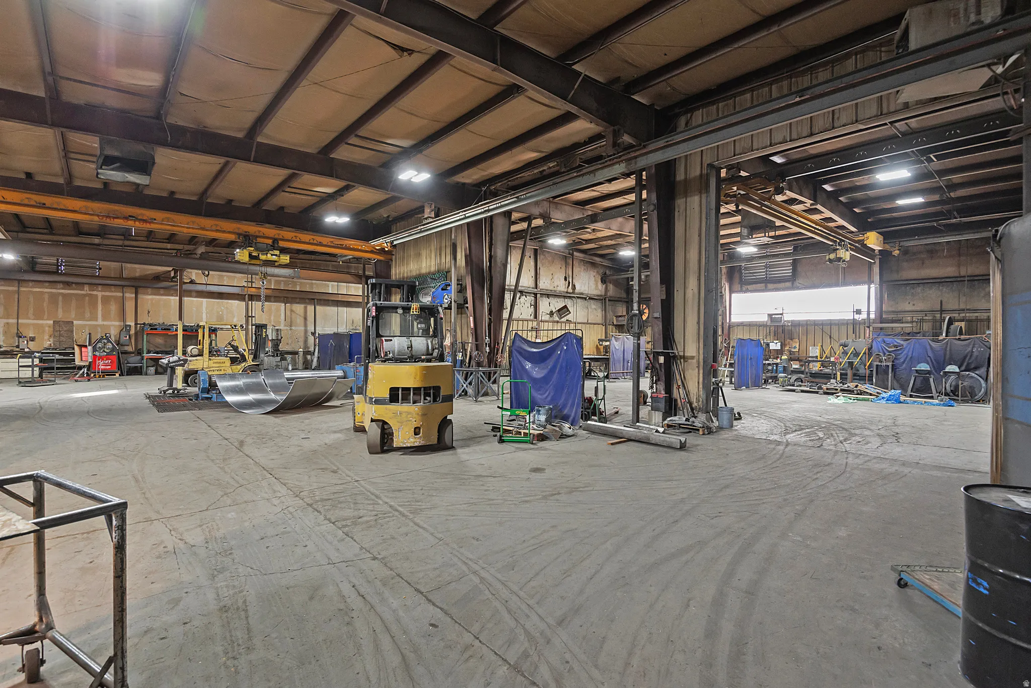 Expansive warehouse space with concrete flooring, overhead crane system, and exposed structural beams