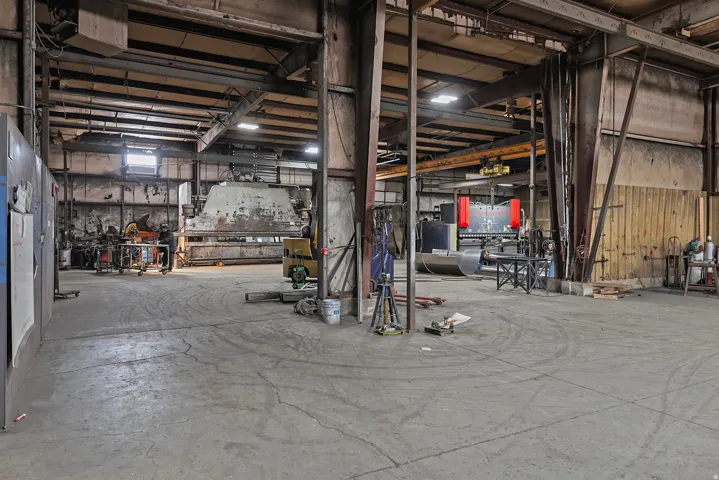 Large industrial space featuring exposed structural beams, concrete flooring, and high ceilings