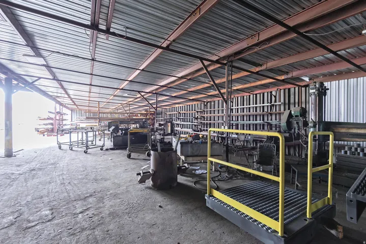 Corrugated metal roof, exposed structural beams, concrete flooring, and extensive open space