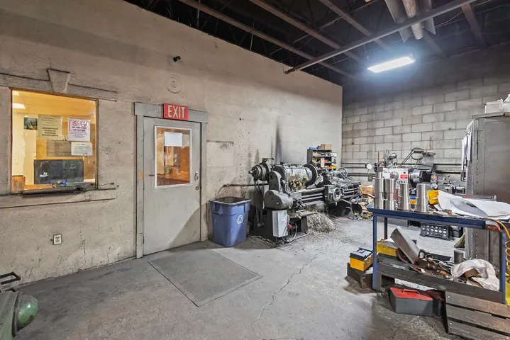 Concrete block walls, exposed ceiling joists, concrete flooring, illuminated light fixture, and a service window