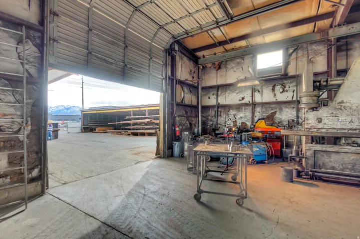 Roll-up door access, concrete flooring, exposed structural elements, overhead lighting, and an industrial-style workspace