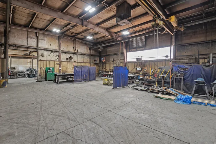 Industrial warehouse space featuring high ceilings, exposed structural beams, overhead lighting, and an overhead crane system