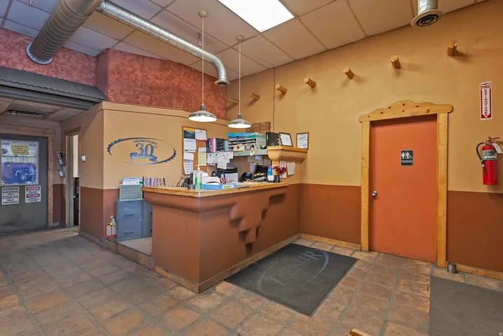 Terracotta tile flooring, exposed ductwork, drop ceiling with fluorescent lighting, built-in reception desk, and solid core doors with wood trim