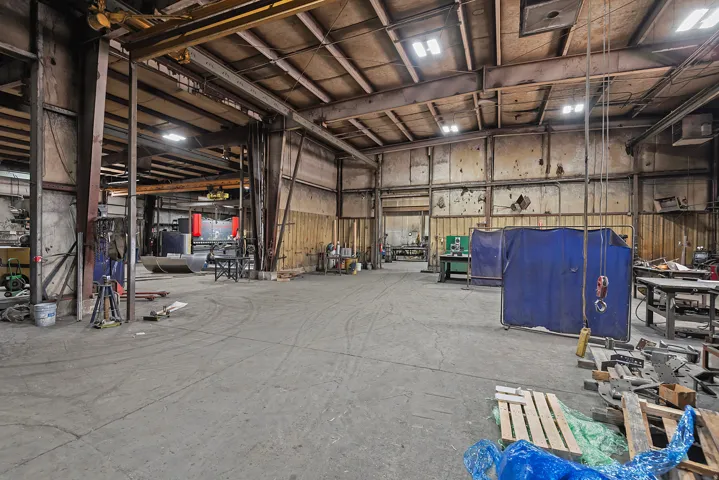 Expansive industrial interior featuring concrete flooring, exposed structural beams, high ceilings, and integrated overhead lighting