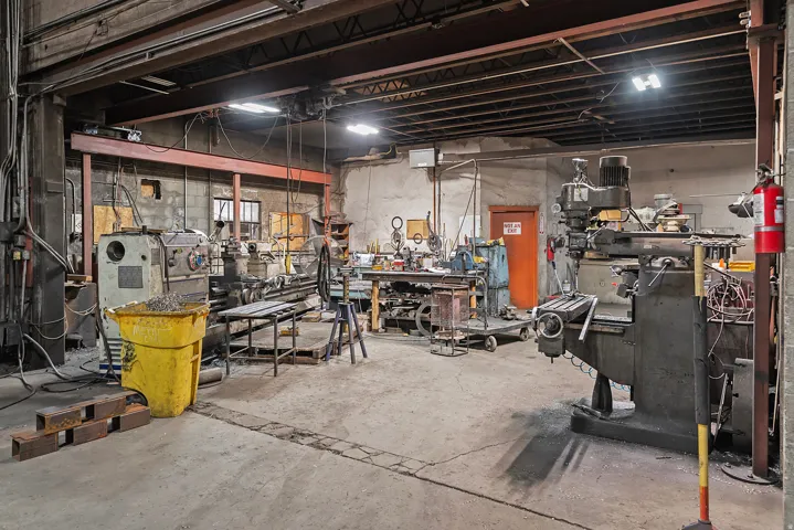 Concrete slab flooring, exposed beam ceiling, raw concrete block walls, overhead lighting, industrial-grade machinery