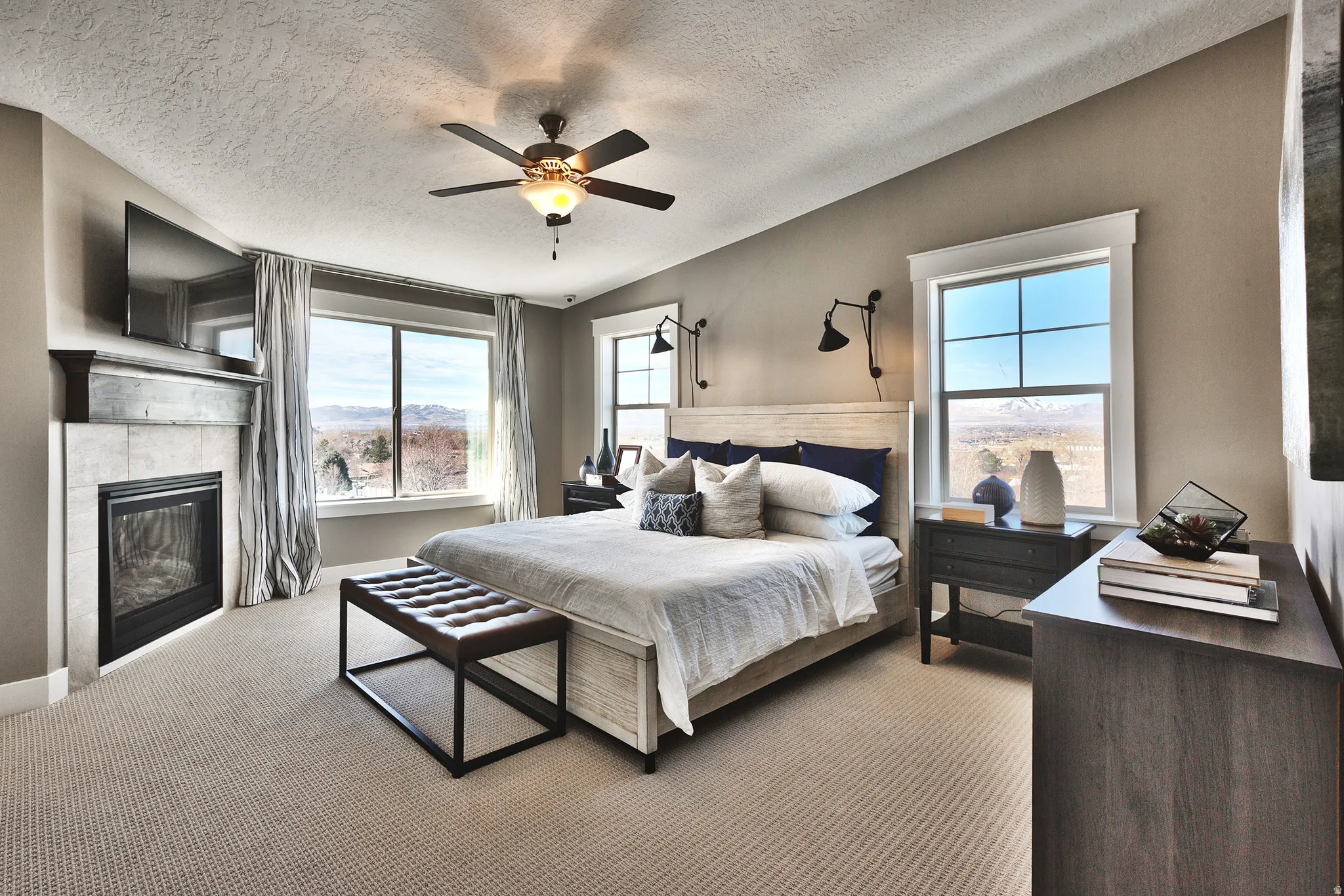 Primary Bedroom, Recessed fireplace with tile surround, ceiling fan with integrated lighting, large windows, and carpet flooring