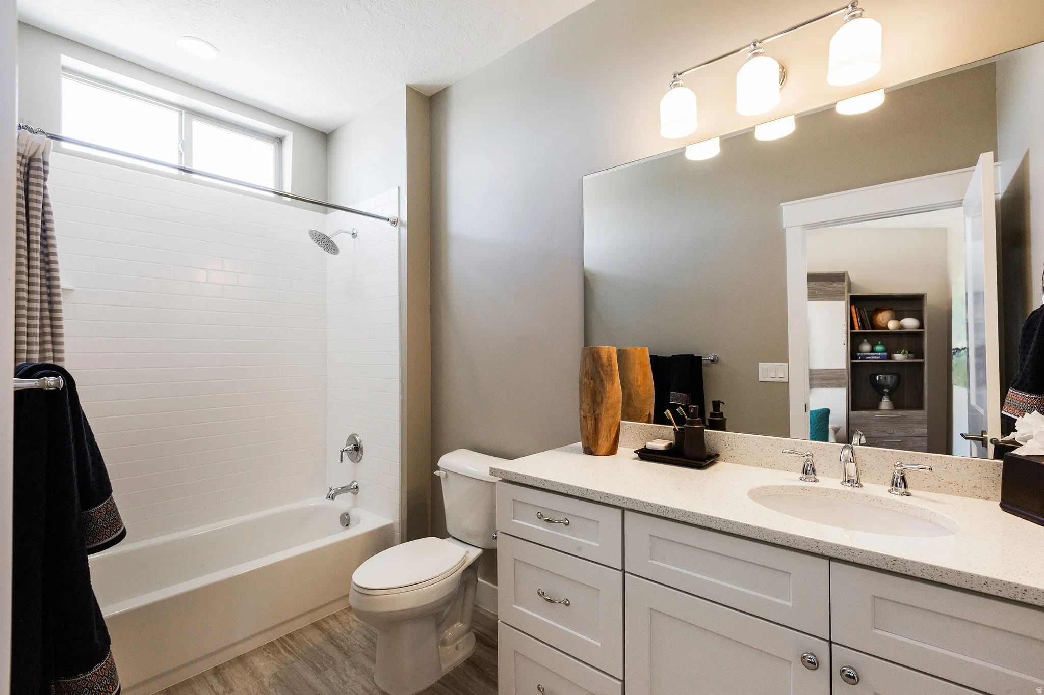 White shaker cabinetry with nickel hardware, light-toned countertop with an integrated sink, large vanity mirror, three-light vanity fixture, and wood-finish flooring