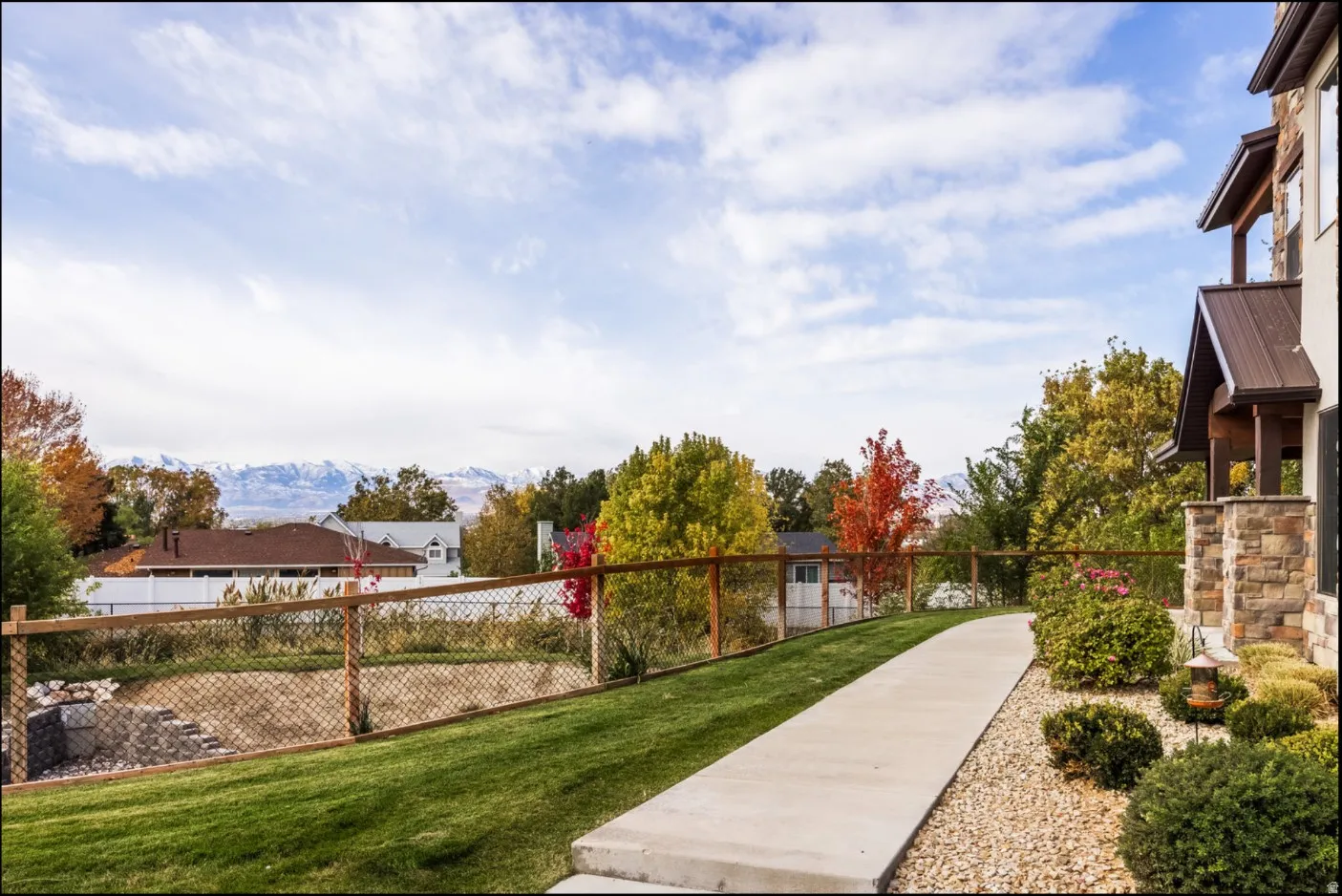 Stone veneer exterior, covered entry with metal roof, concrete pathway, gravel landscaping, and wood-frame fencing