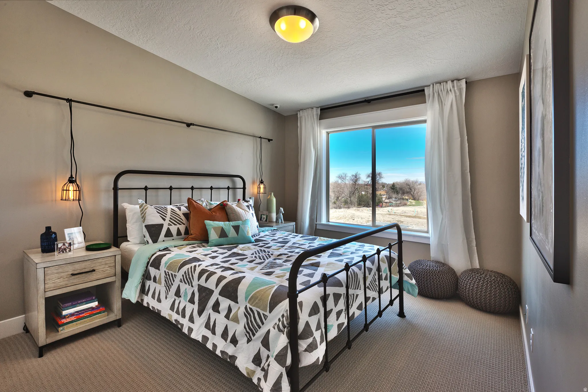 Carpeted flooring, window with exterior scenery, wall-mounted light fixtures, built-in ceiling light, and a nightstand with a drawer