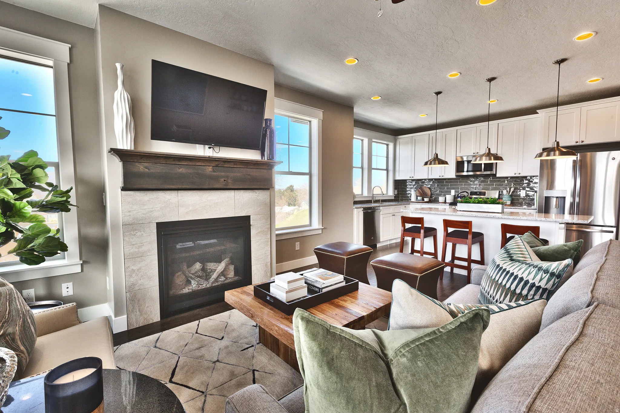 Living area featuring a gas fireplace with a wood mantel, tile surround, and a kitchen with white cabinetry, stainless steel appliances, and a central island with bar seating