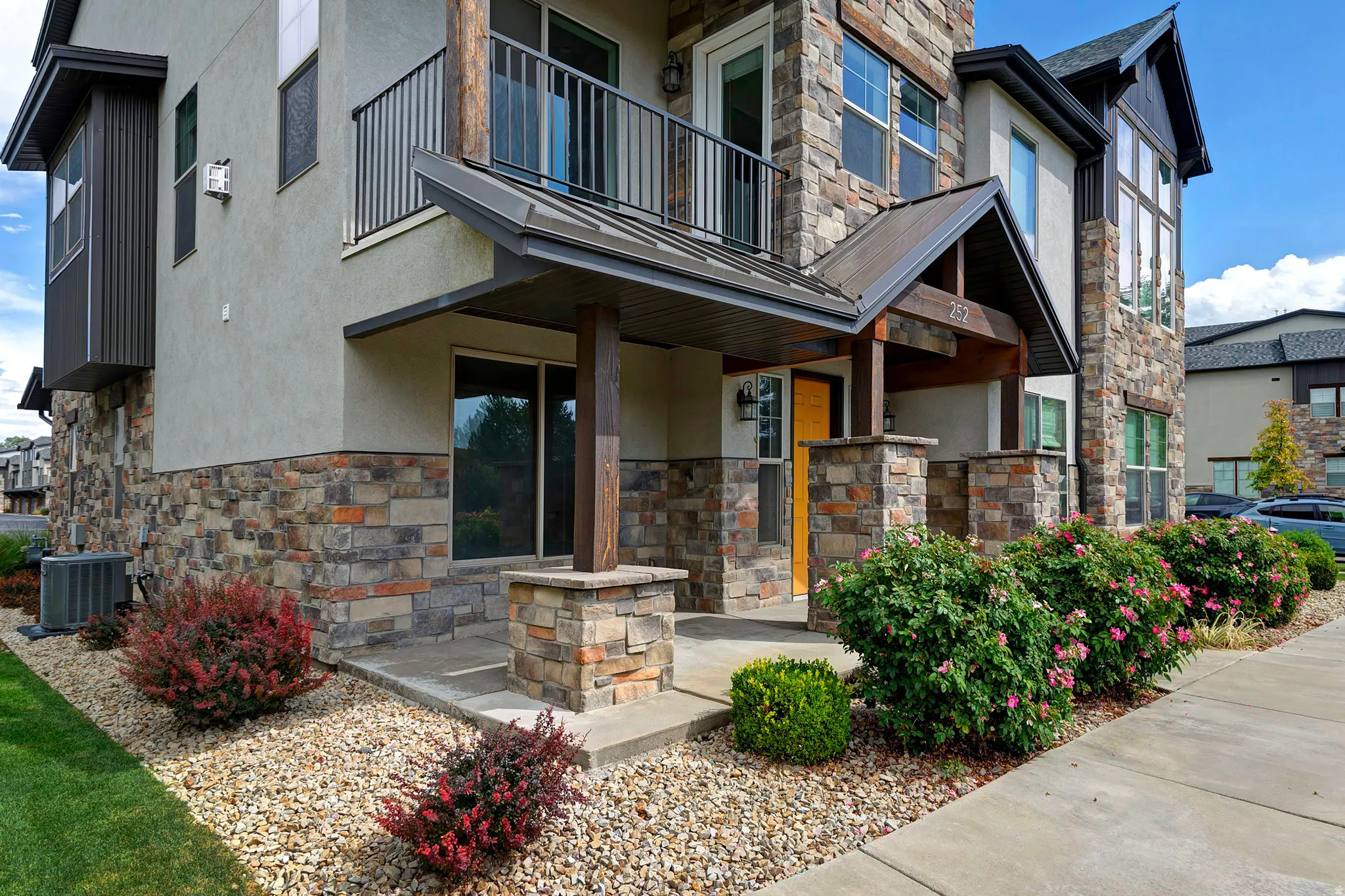 Multi-level stucco and stone facade featuring a covered entry, an upper-level balcony with metal railings, and a prominent stone chimney