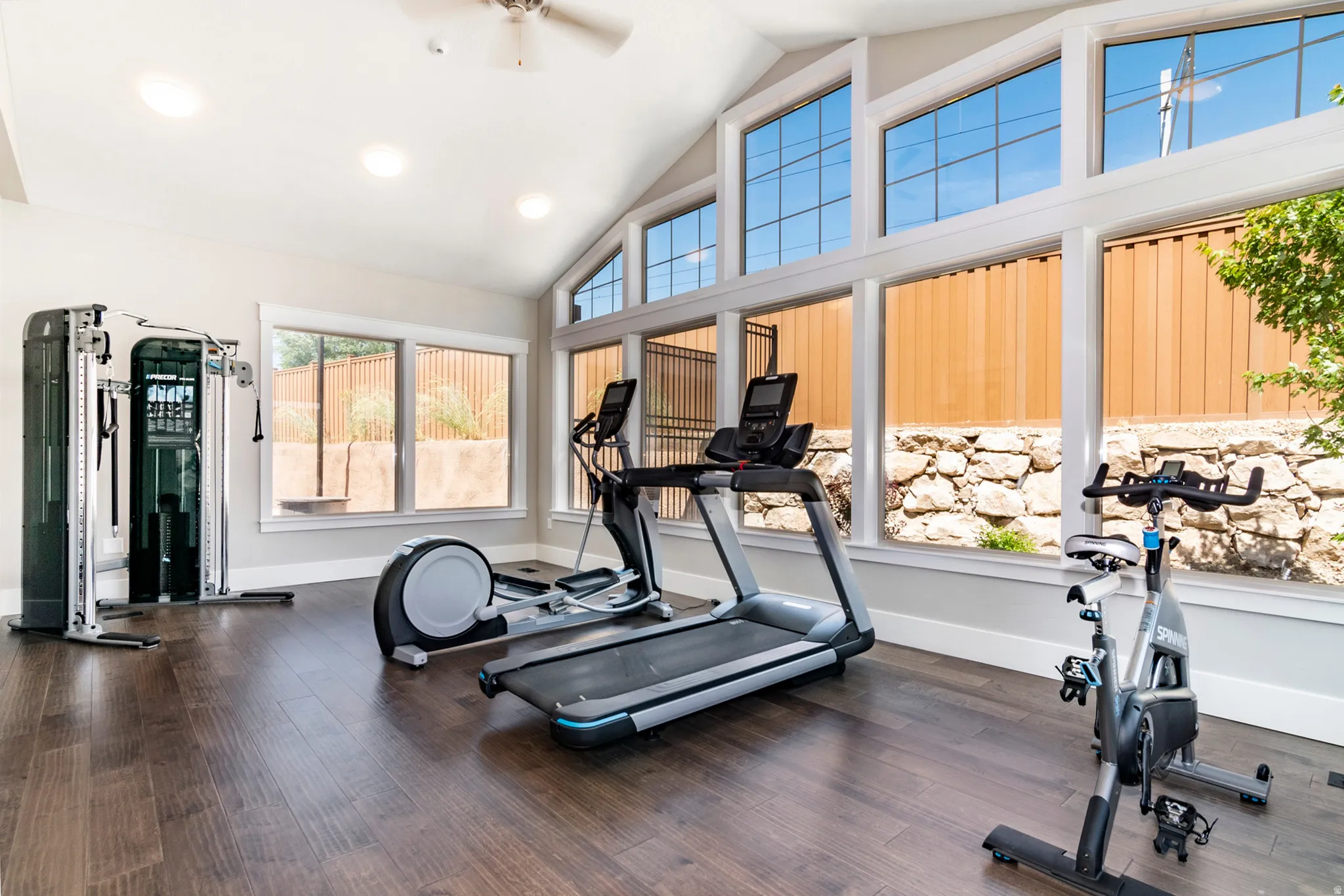 Vaulted ceilings with a ceiling fan, recessed lighting, expansive windows, wood-finish flooring, and a stone retaining wall