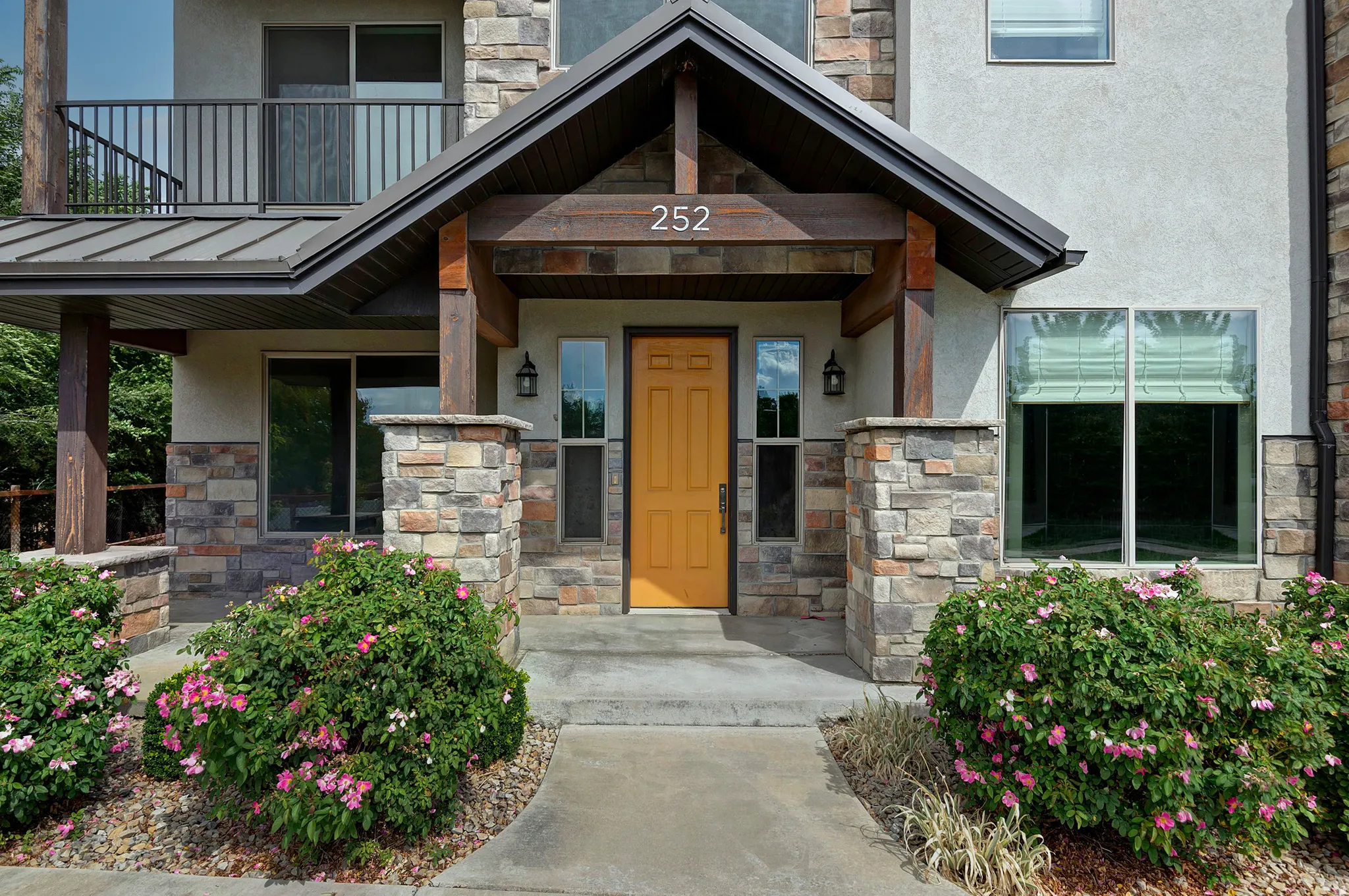 Stone veneer accents, prominent entry door, covered entry, second-story balcony with metal railing, and a gabled roofline