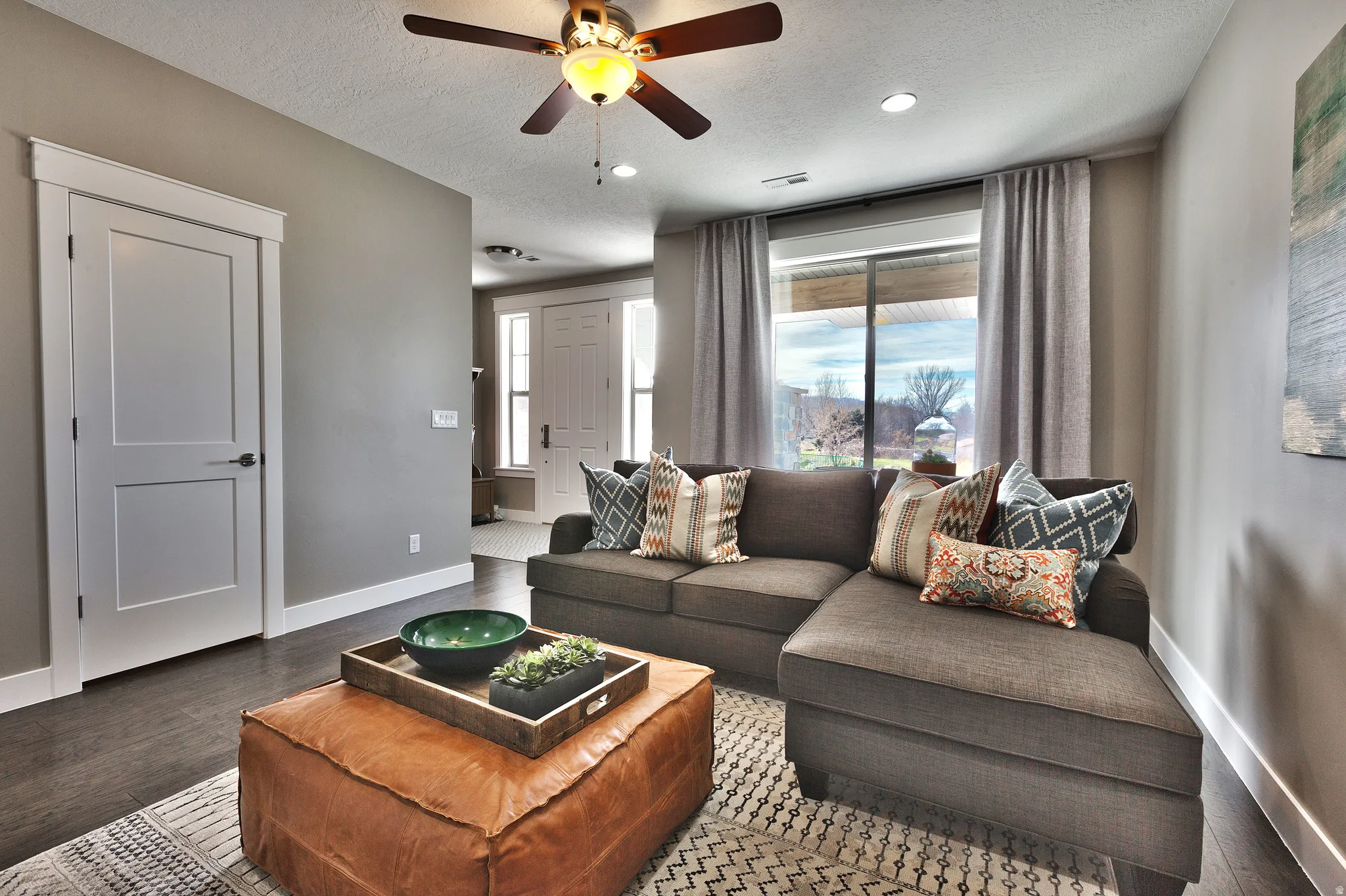 Dark wood-finish flooring, recessed ceiling lighting, a ceiling fan with integrated light, and a sliding glass door