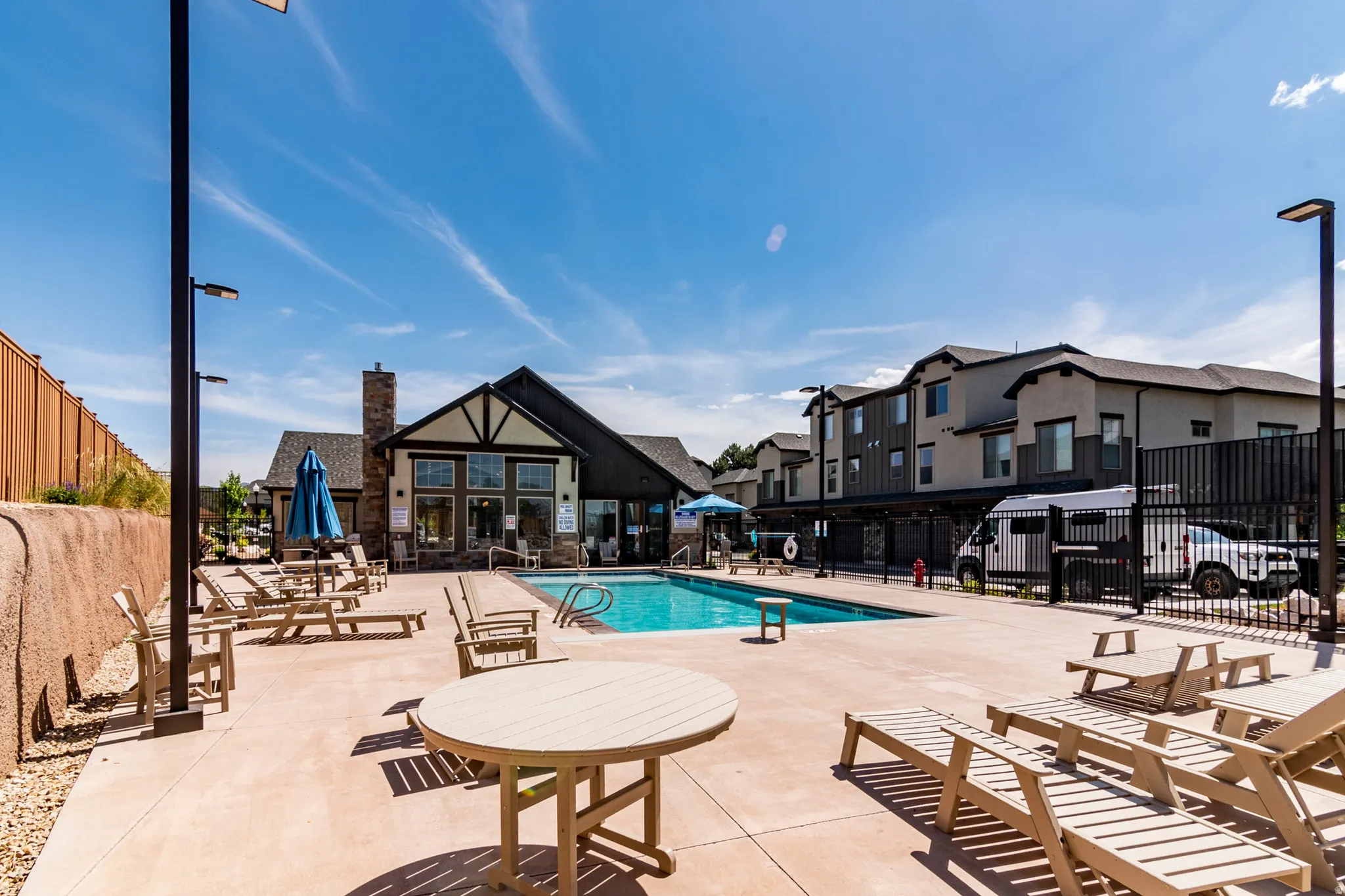 Community pool with expansive hardscaping, surrounded by multi-story residential buildings and a clubhouse structure featuring a stone chimney