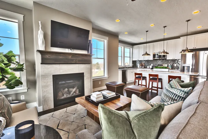 Living area featuring a gas fireplace with a wood mantel, tile surround, and a kitchen with white cabinetry, stainless steel appliances, and a central island with bar seating