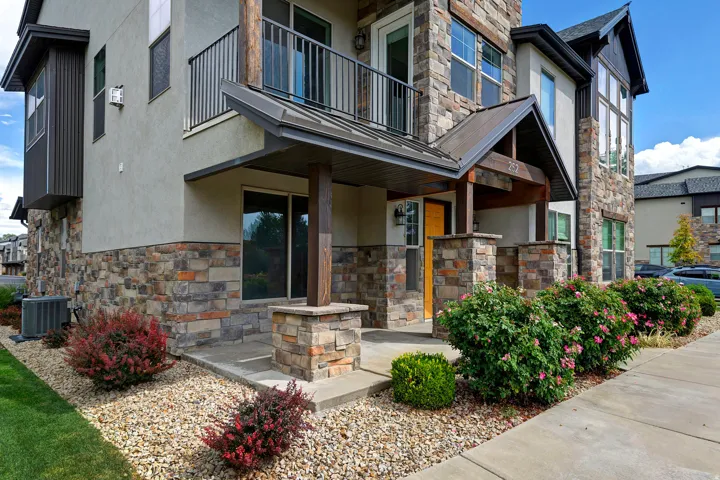 Multi-level stucco and stone facade featuring a covered entry, an upper-level balcony with metal railings, and a prominent stone chimney