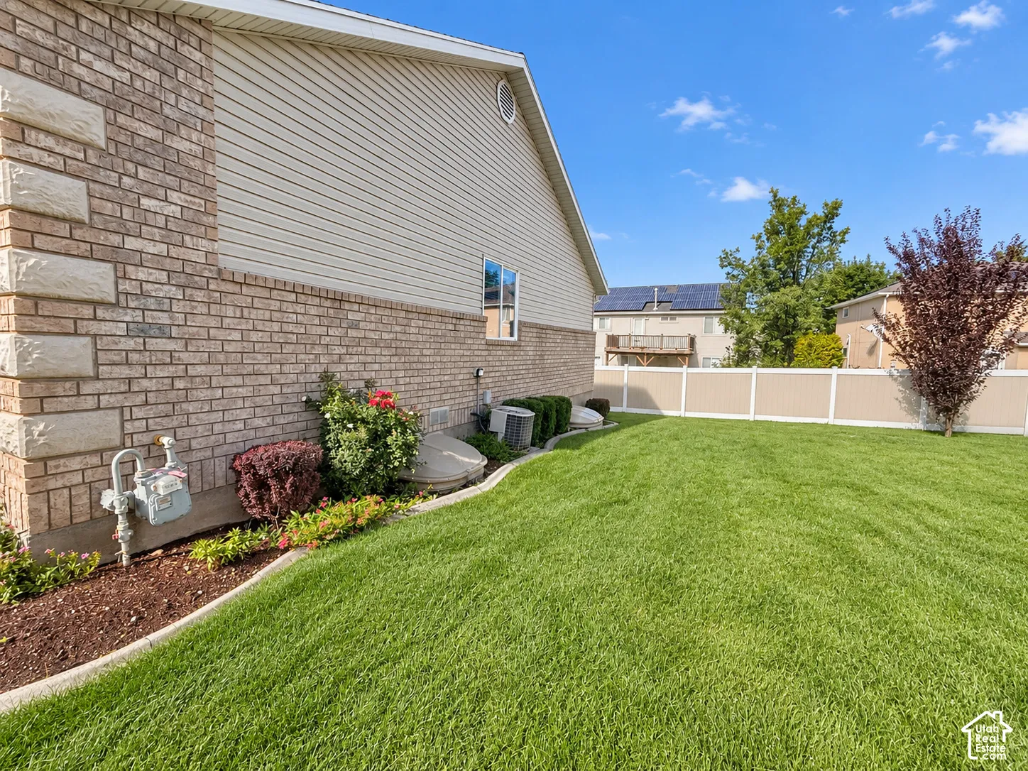 Expansive lawn with a two-tone privacy fence, brick exterior, and decorative shrubbery