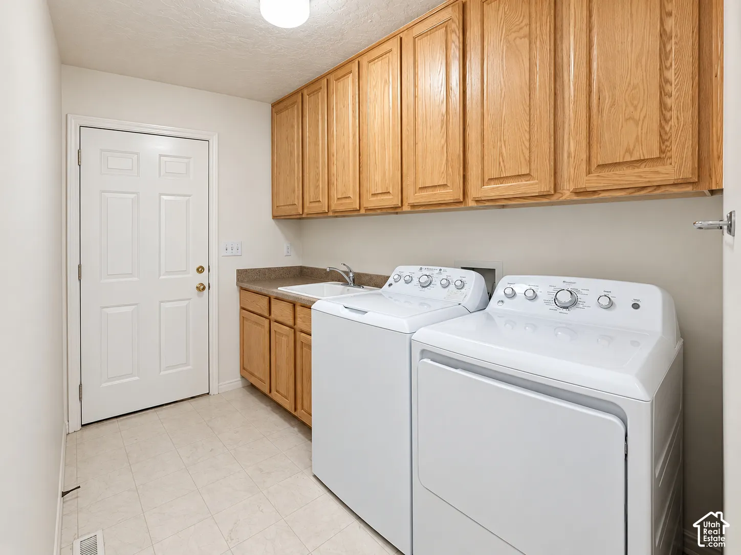 Laundry area featuring wood cabinetry, a utility sink, and durable tile flooring