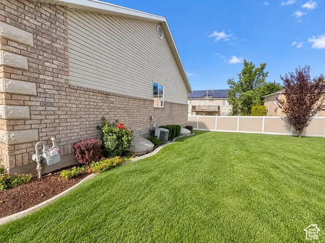 Expansive lawn with a two-tone privacy fence, brick exterior, and decorative shrubbery