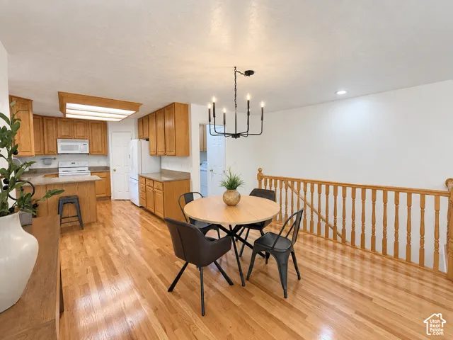 Wood-finish flooring throughout, kitchen with wood cabinetry and light-toned countertops, kitchen island, white appliances, and a black chandelier