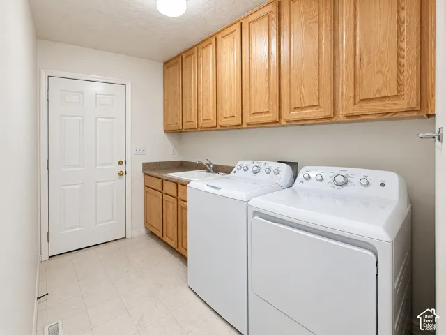 Laundry area featuring wood cabinetry, a utility sink, and durable tile flooring