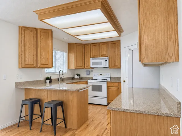 Kitchen featuring wood cabinetry, stone-finish countertops, wood-finish flooring, white appliances, and an island with counter seating