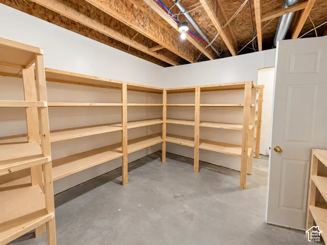 Concrete flooring with extensive built-in wooden shelving, exposed ceiling joists, and a paneled door