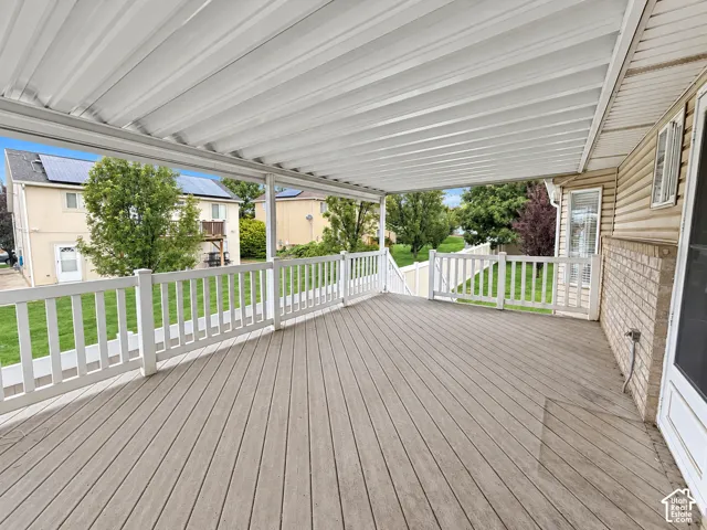 Spacious covered deck featuring composite decking and white railing, complemented by a vinyl siding exterior with brick accents