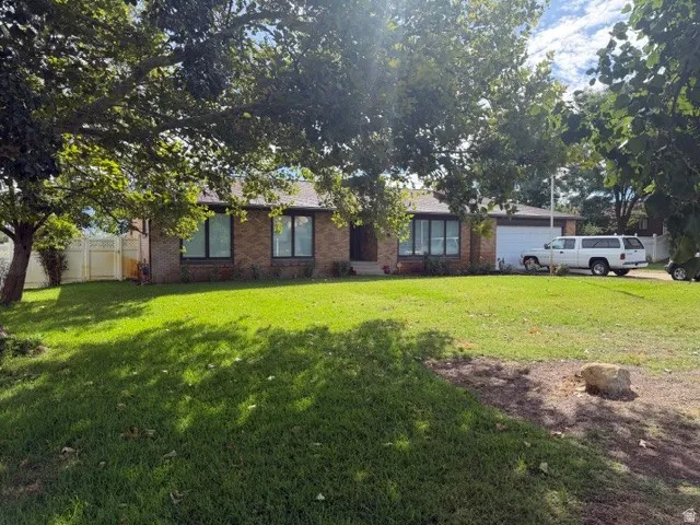 Brick exterior with a single-car garage, mature trees, and a spacious green lawn
