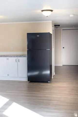 Wood-finish flooring throughout, white cabinetry with silver hardware, and a black refrigerator