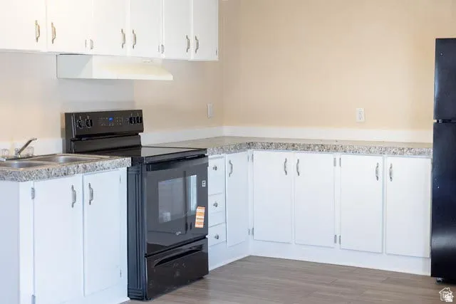 White cabinetry, dark wood-finish flooring, dark appliance suite, light-toned walls, and speckled countertops