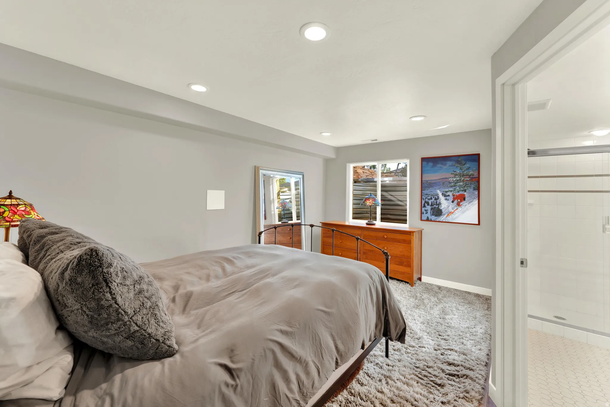 Recessed lighting, wood-finish dresser, white trim, and a full bathroom featuring a glass-enclosed shower with tile surround and hexagon tile flooring