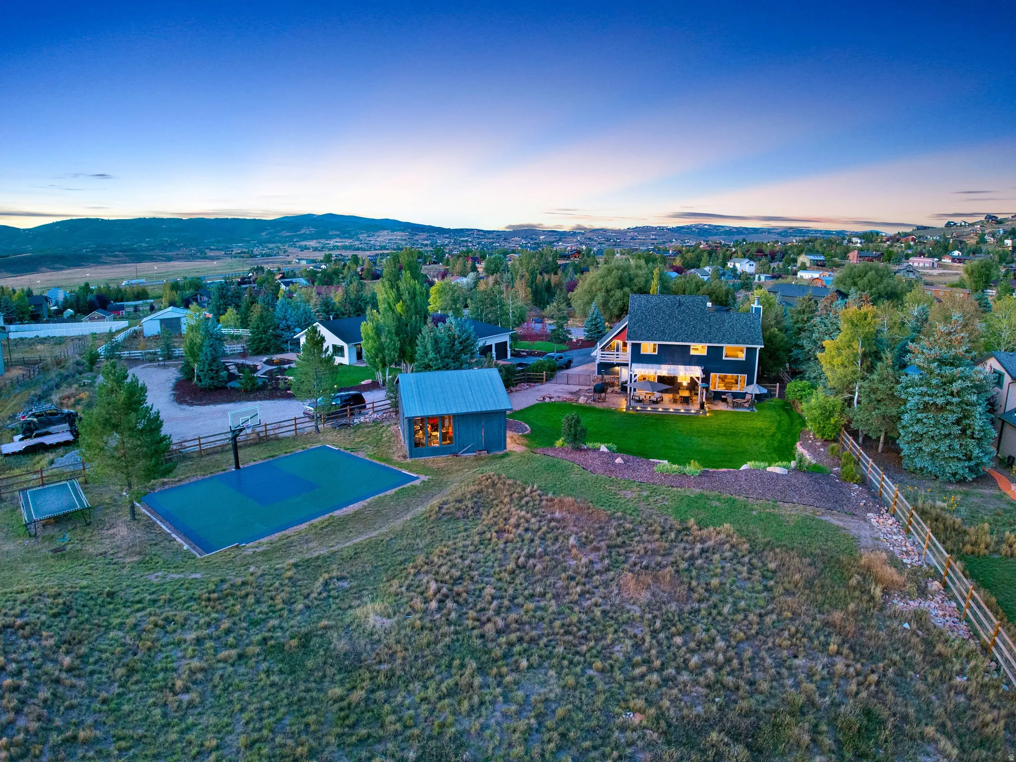 Expansive property featuring a multi-sport court, detached shed, upper-level deck, lower-level patio, and surrounding mountainous terrain