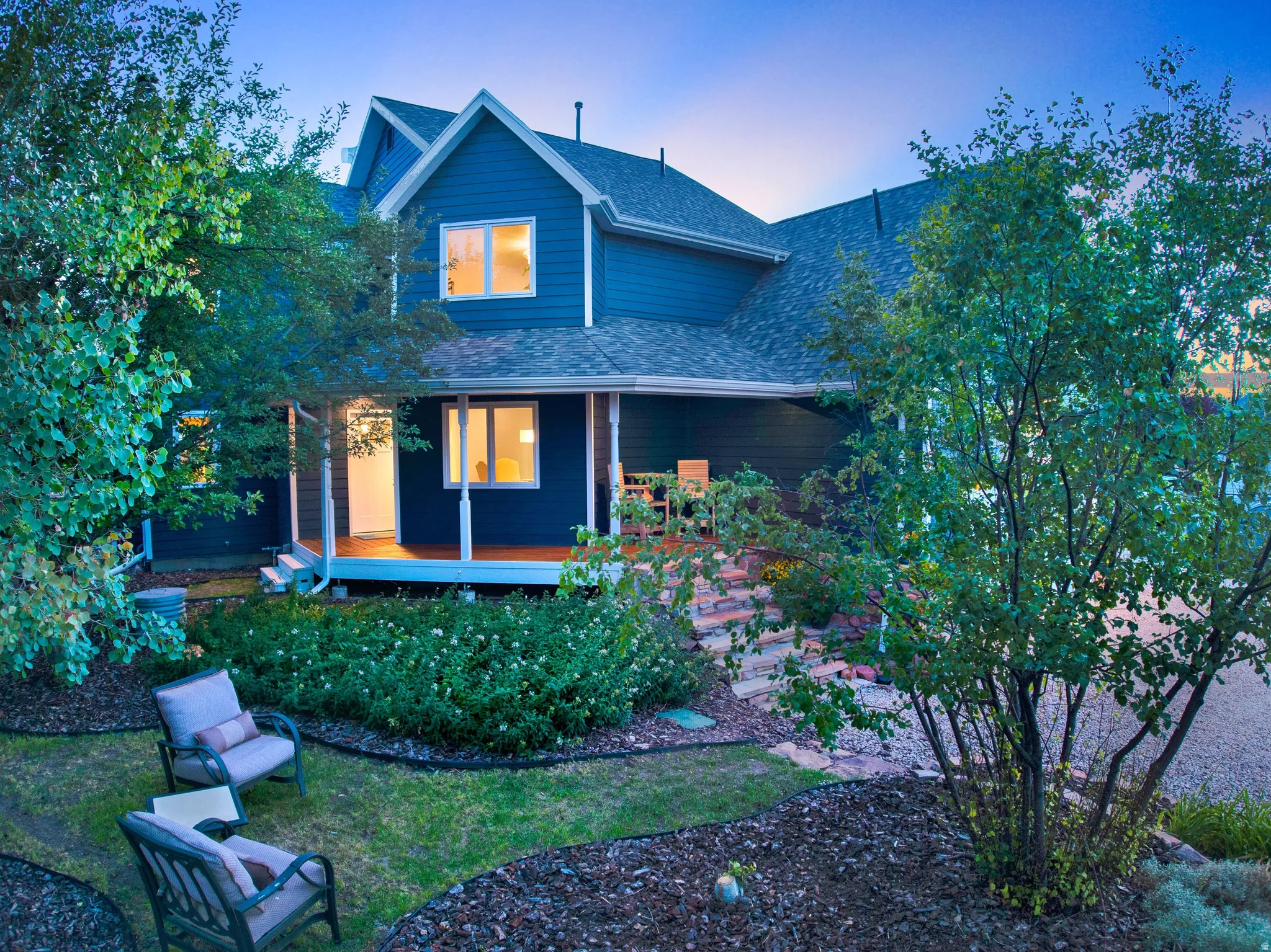 Blue exterior siding, gable roofline, covered porch with columns, stone steps, and landscaped grounds