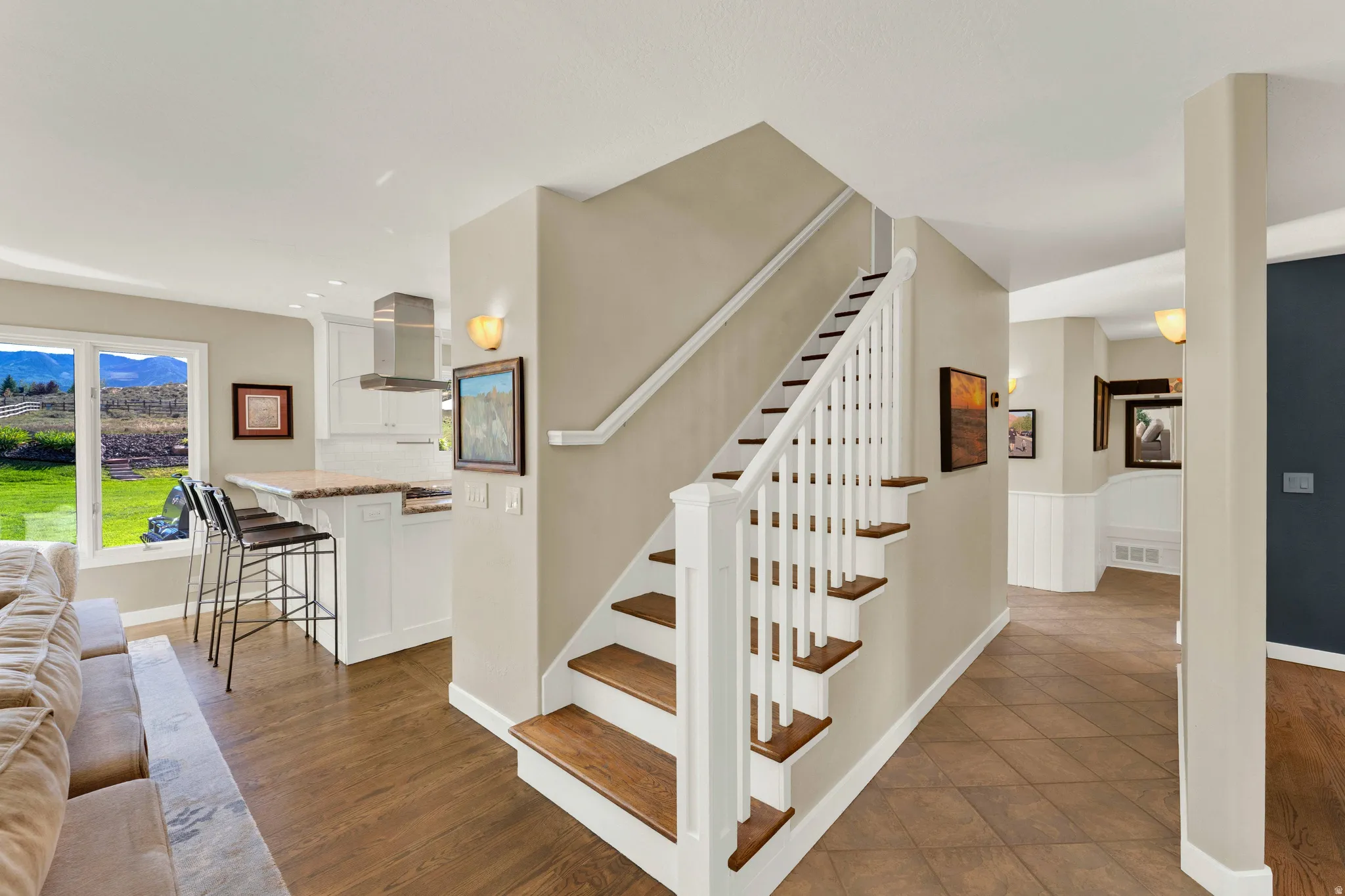 Wood-finish flooring, staircase with white risers and balusters, white cabinetry, stainless steel range hood, and a breakfast bar with stone-finish countertop
