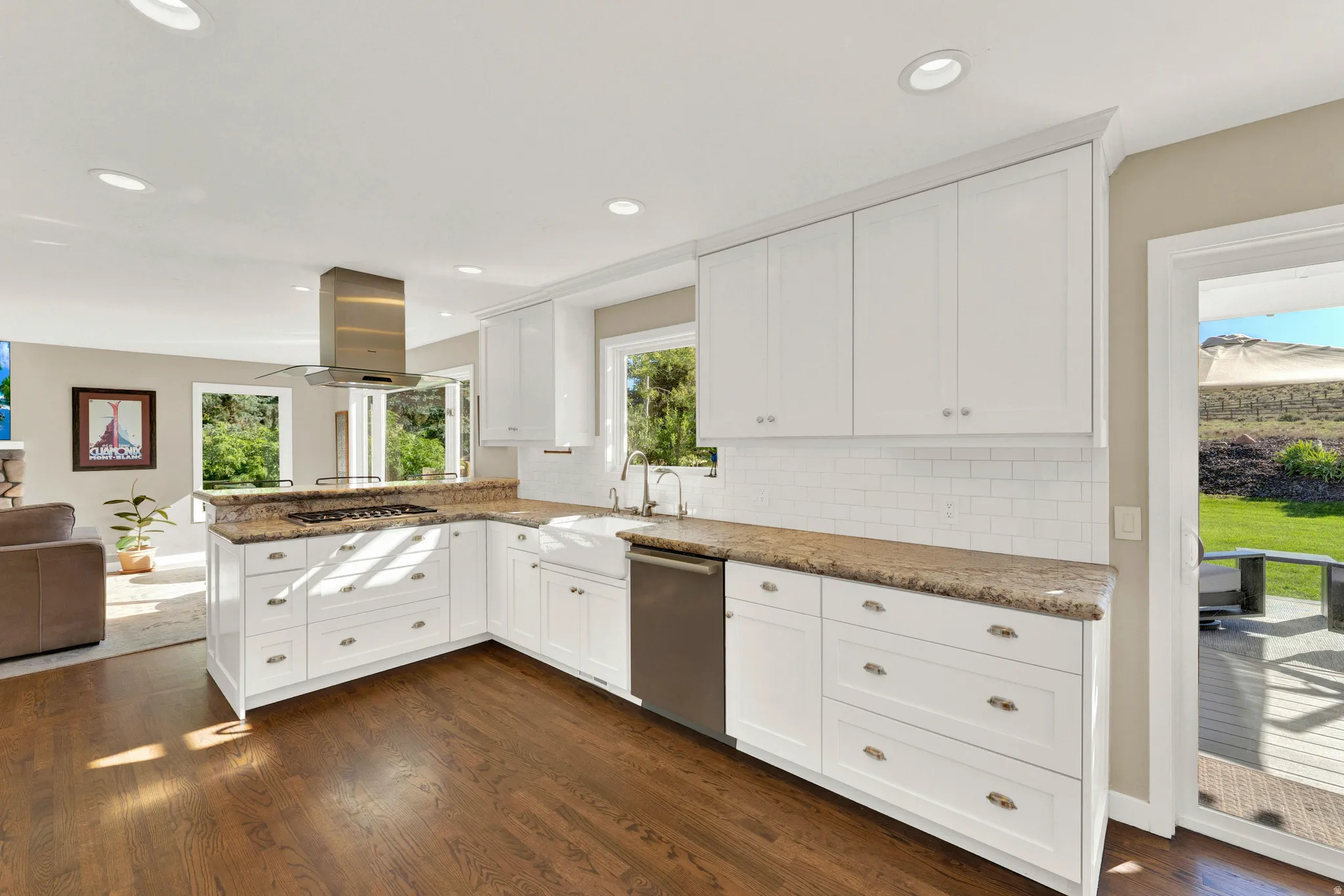 White shaker cabinetry, wood-finish flooring, stainless steel appliances, farmhouse sink, and a tile backsplash