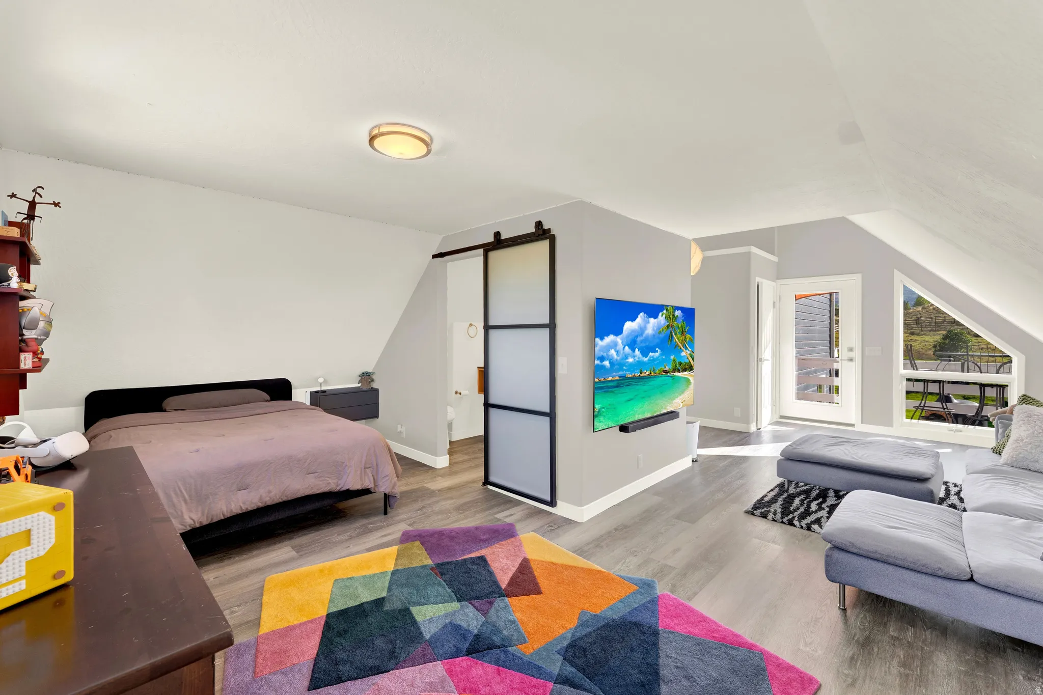 Vaulted ceilings, wood-finish flooring, sliding barn door, wall-mounted light fixture, and an exterior door with glass paneling