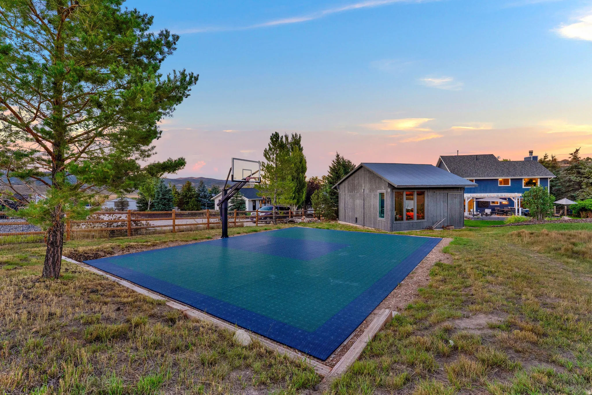 Outdoor sports court with a basketball hoop, detached outbuilding, and a two-story residence with an attached pergola