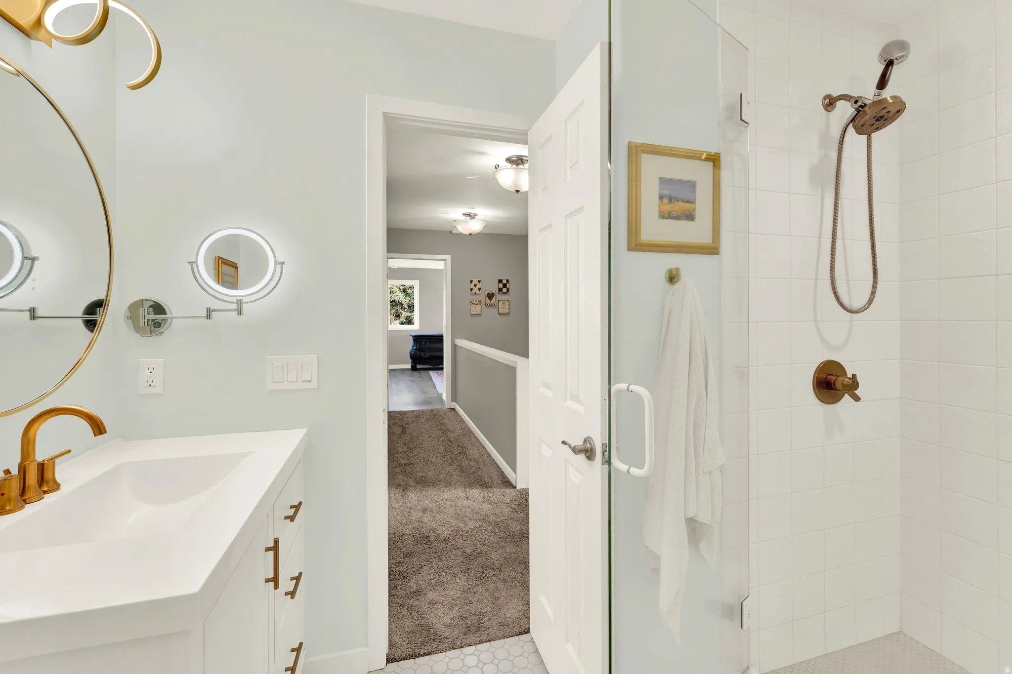 Bathroom featuring a white vanity, integrated sink, gold-finish faucet, and a large round mirror