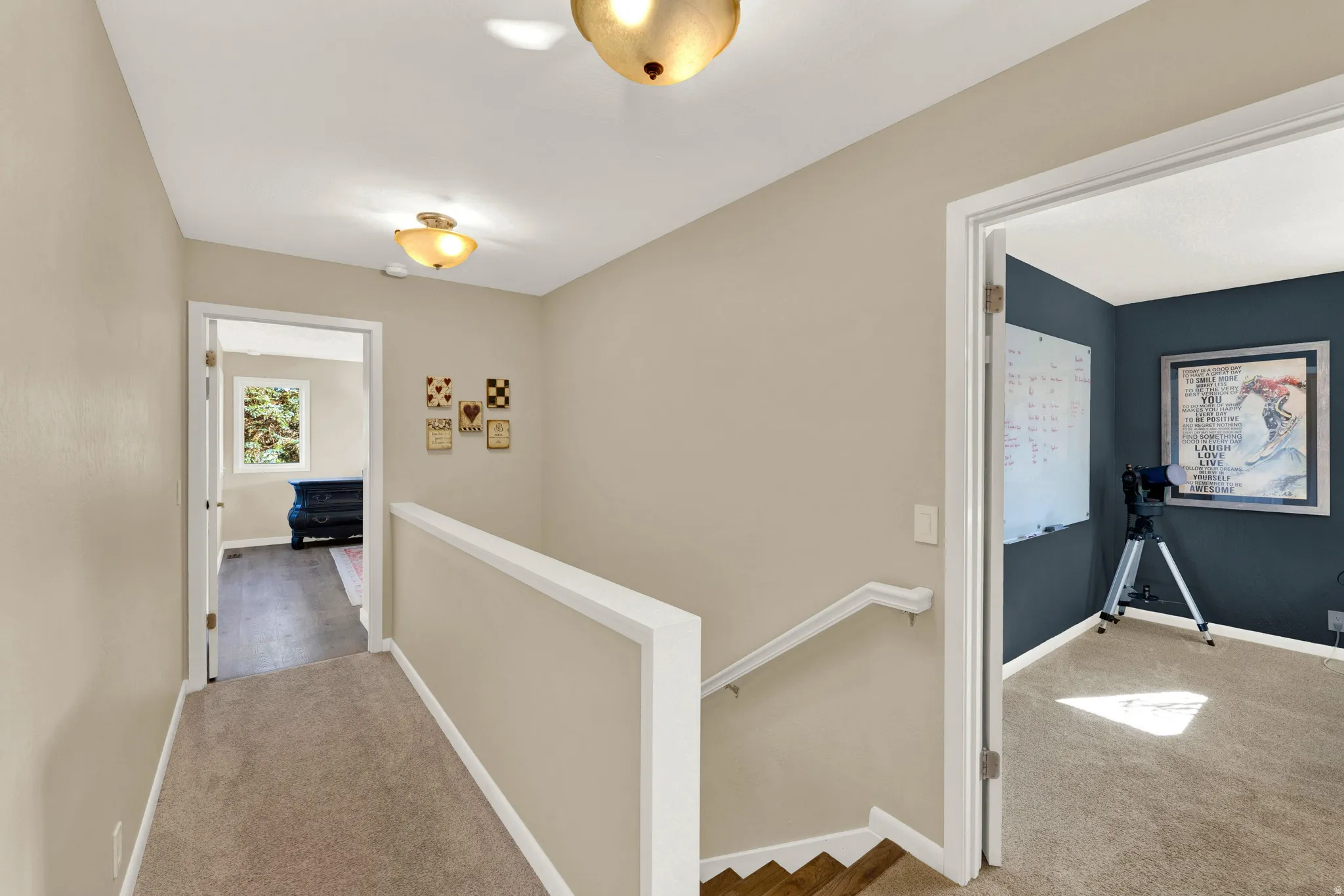 Upper-level hallway featuring neutral wall paint, carpeted flooring, two flush-mount light fixtures, and a white railing