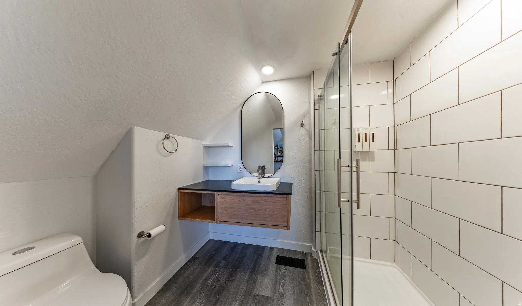 Floating vanity with a vessel sink, dark countertop, and wood-finish cabinetry
