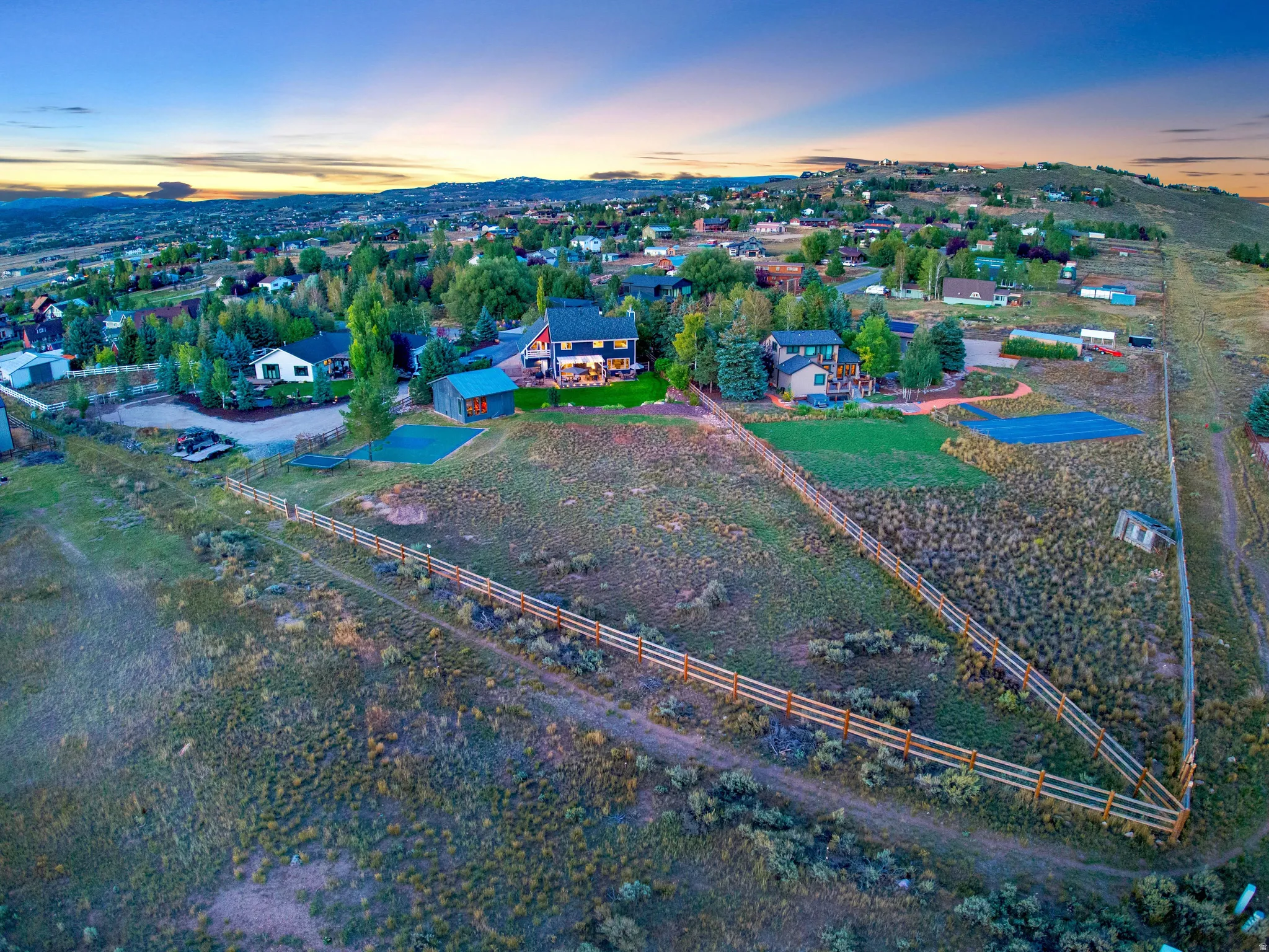 Expansive property featuring a multi-rail fence, scattered trees, and a distant residential community