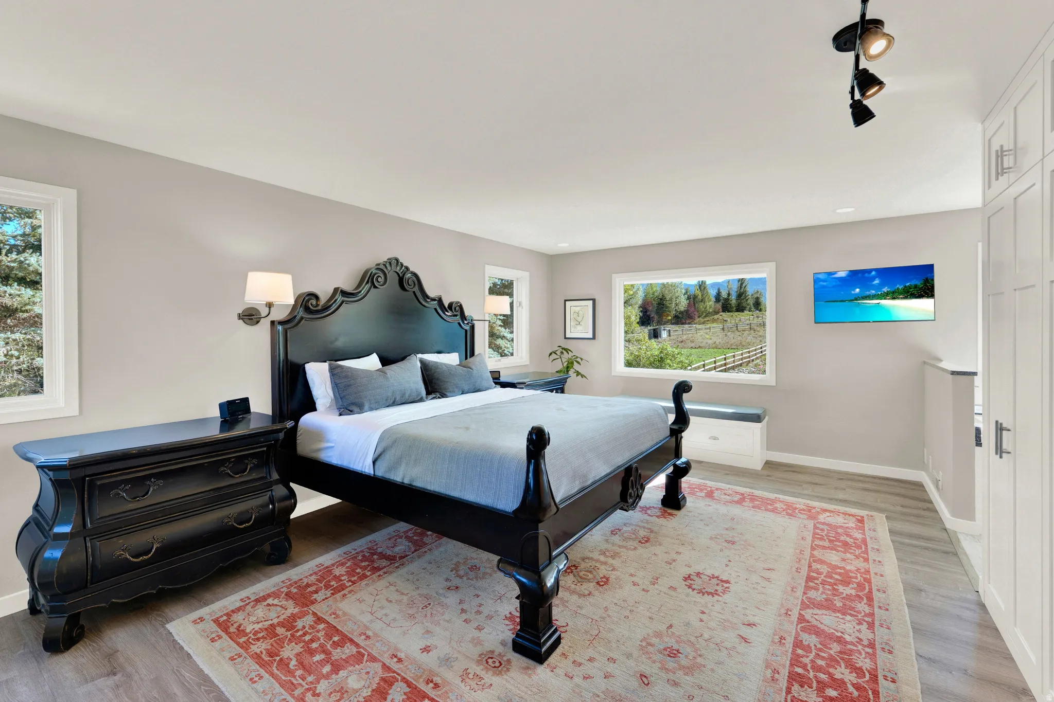 White framed windows, light-toned walls, wood-finish flooring, built-in cabinetry, and ceiling-mounted track lighting