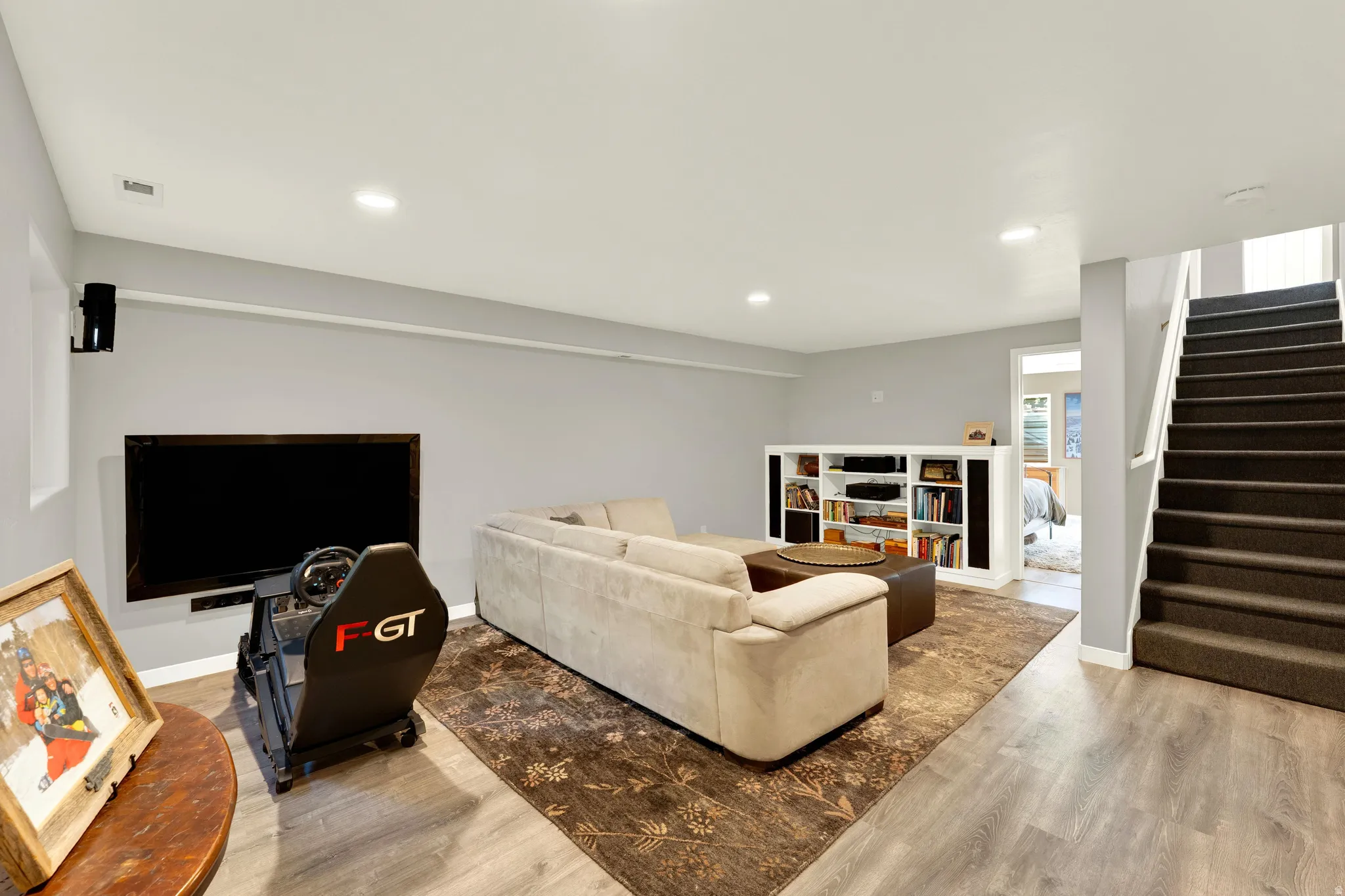 Recessed lighting illuminates the open-concept living space, featuring wood-finish flooring and a built-in shelving unit
