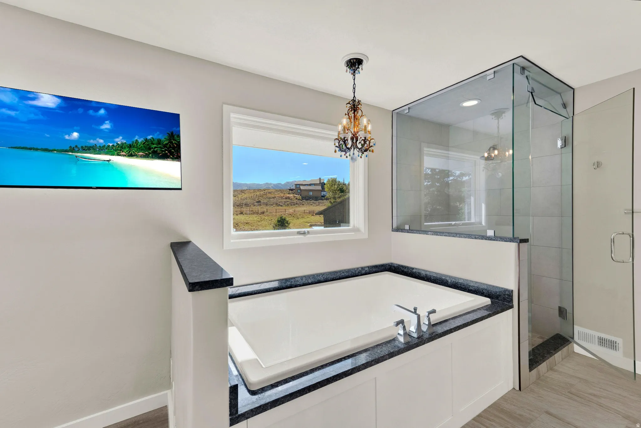 Built-in soaking tub with granite surround, separate glass-enclosed shower, and a decorative chandelier